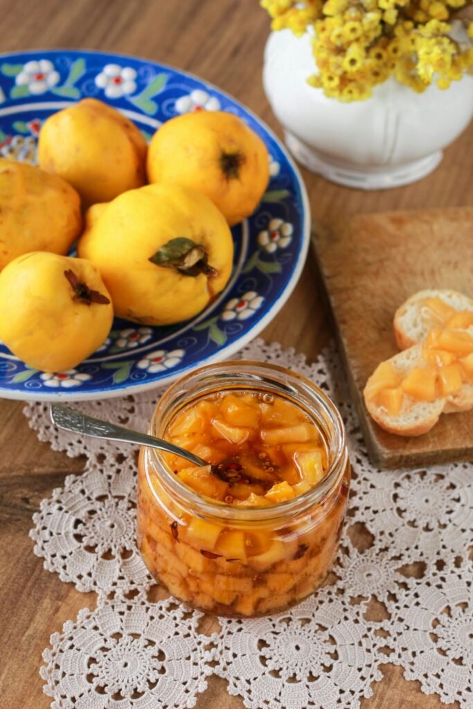 Homemade quince jam in a jar with quince fruits and toast on a wooden table.